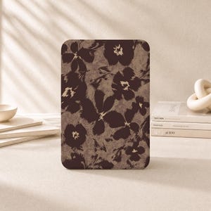 Op de afbeelding: Een rechthoekige tablethoes met een donkerbruin bloemenpatroon op een getextureerde beige achtergrond. Het ontwerp bestaat uit gestileerde, abstracte bloemvormen met zichtbare penseelstreekdetails die de gehele voorzijde van de hoes bedekken.