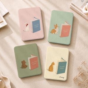 May include: Four rectangular notebooks with rounded corners. The pink one features a white rabbit and a blue book. The green one shows a corgi and a red book. The olive one displays a brown bear and a red book. The cream one has a cat and a blue book.