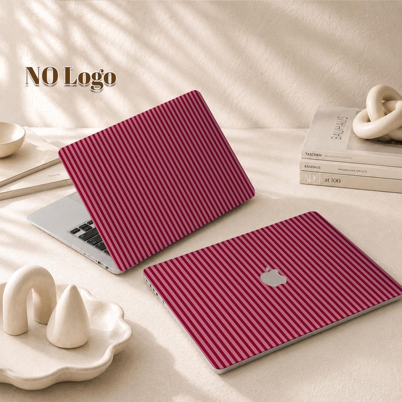 Peut inclure: Un autocollant pour ordinateur portable avec un motif de fines rayures verticales rouge fonc&eacute; et rose clair. Un ordinateur est ouvert avec l'autocollant sur le couvercle, et un autre est ferm&eacute;, montrant le m&ecirc;me motif ray&eacute; et un logo pomme argent&eacute;.