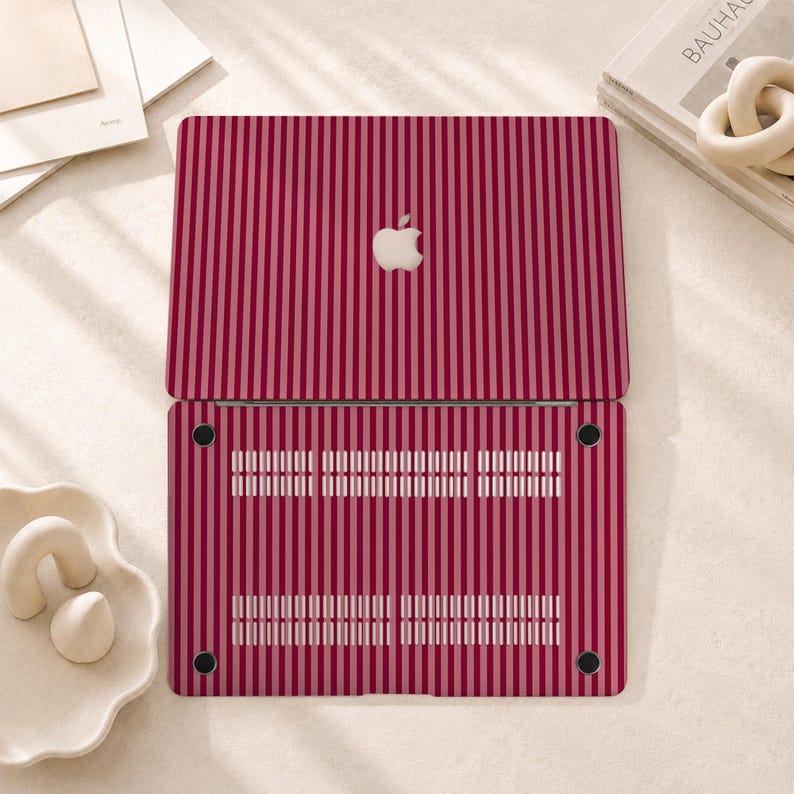 Peut inclure: Une coque rigide pour ordinateur portable avec un motif &agrave; rayures verticales dans des tons altern&eacute;s de rouge fonc&eacute; et de rose clair. La partie sup&eacute;rieure pr&eacute;sente une d&eacute;coupe centrale pour le logo Apple, tandis que la base comporte des fentes d'a&eacute;ration.