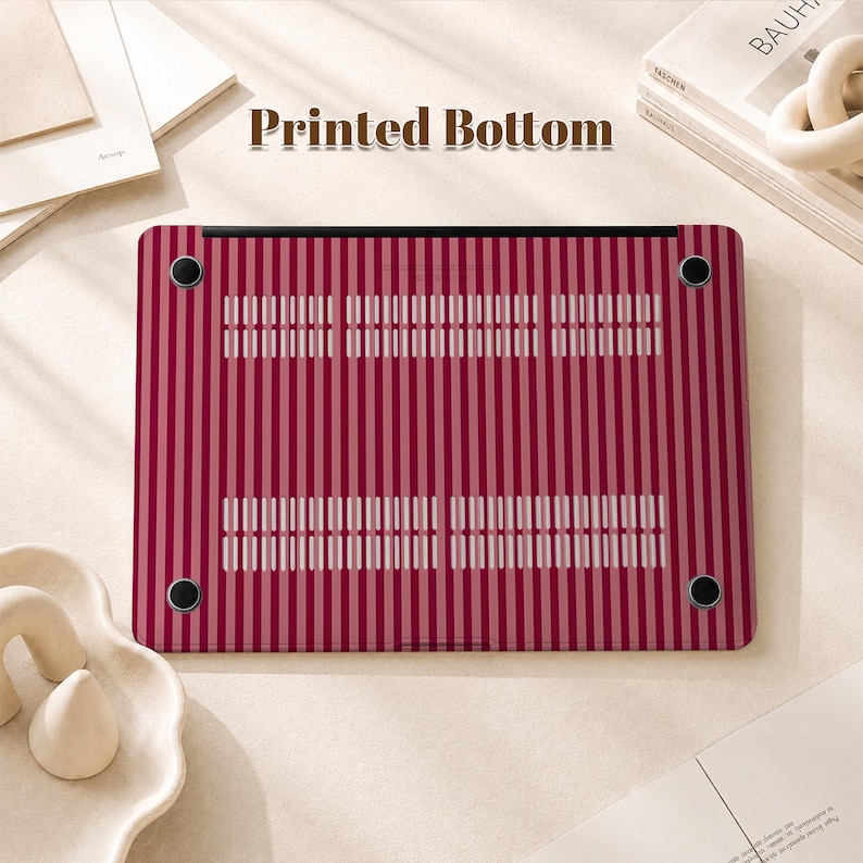 Peut inclure: Une coque rigide rectangulaire pour ordinateur portable avec un motif &agrave; rayures verticales dans des tons rouge fonc&eacute; et rose clair. La coque comprend quatre pieds en caoutchouc noir circulaires aux coins et deux fentes d'a&eacute;ration.