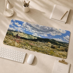 May include: A rectangular desk mat featuring an impressionistic landscape painting of a vast field with tall grasses, rolling green hills, a dark forest line, and a bright blue sky filled with large, textured white clouds.