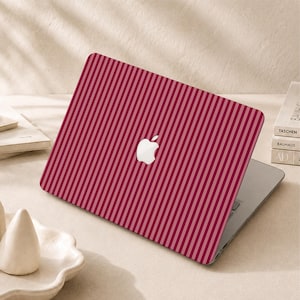Peut inclure: Un ordinateur portable dot&eacute; d'une coque de protection &agrave; rayures verticales alternant des tons rouge fonc&eacute; et rose clair. Le logo Apple blanc est visible au centre du couvercle, qui est ferm&eacute; et pos&eacute; sur une surface plane.