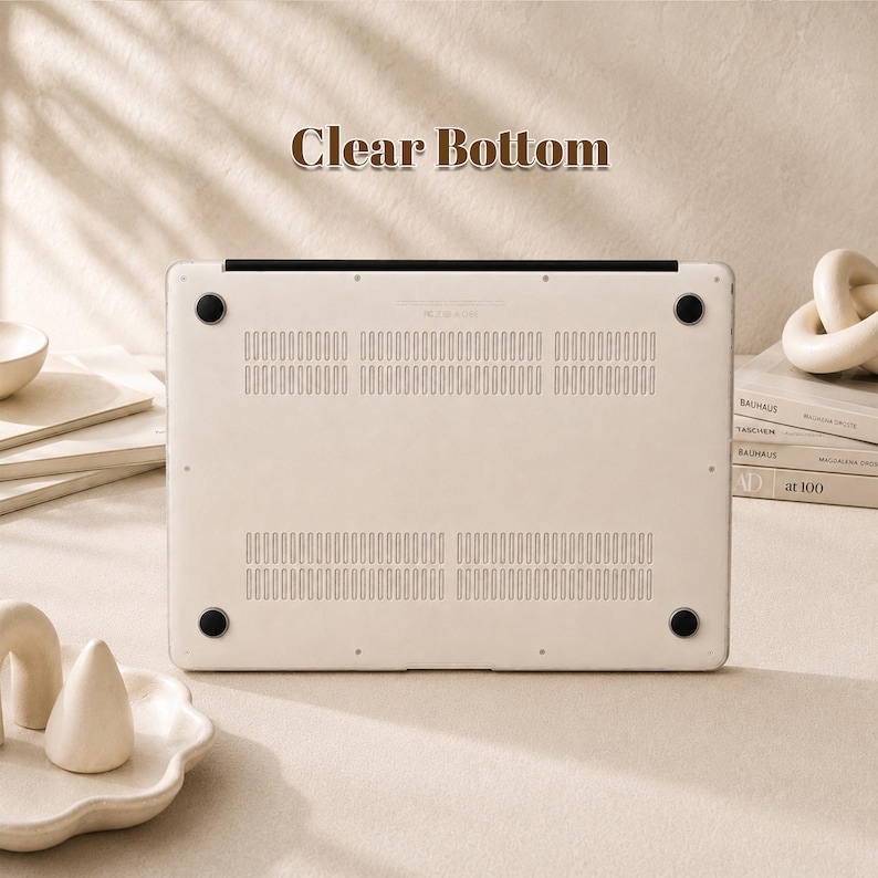 Peut inclure: Une coque de protection transparente pour ordinateur portable, de forme rectangulaire, dot&eacute;e de fentes d'a&eacute;ration et de quatre pieds circulaires noirs en caoutchouc. Le texte Clear Bottom est imprim&eacute; au-dessus de la coque de protection.