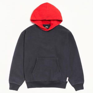 Puede incluir: Una sudadera con capucha de manga larga en color gris carbón que presenta una capucha de color rojo vibrante, un bolsillo tipo canguro frontal y una pequeña etiqueta de marca blanca en el lado inferior derecho. El interior de la capucha es rojo.