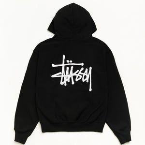 May include: A black long-sleeve hooded sweatshirt featuring a large white Stüssy logo printed on the back. The garment includes a hood, long sleeves with ribbed cuffs, and a ribbed hem, showcasing a clean design with the brand name in white.