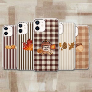 Peut inclure: Cinq coques de téléphone avec des motifs d'automne. La première a des rayures brunes et des citrouilles. La deuxième a des rayures brunes et une feuille d'érable. La troisième a un motif vichy brun avec un pot de pumpkin spice. La quatrième a des rayures et des feuilles. La cinquième a un motif vichy beige et un gland.
