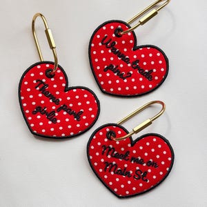May include: Three heart-shaped red patches with white polka dots and black embroidered text. Each patch features a gold-toned metal locking pin loop. The text reads: Theme park girlie, Wanna trade pins?, and Meet me on Main St. in black thread.