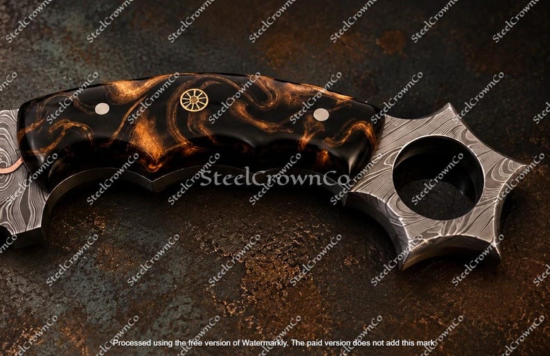 Puede incluir: Un cuchillo curvo con un mango de patr&oacute;n jaspeado en negro y cobre, asegurado por dos remaches plateados y un emblema central de rueda dorada. La hoja muestra un patr&oacute;n distintivo de acero de Damasco con un orificio circular para el dedo.