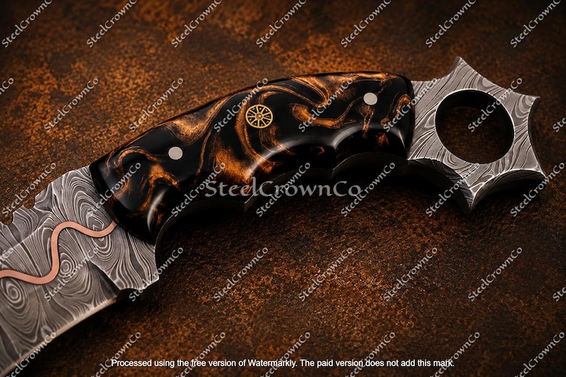Puede incluir: Un cuchillo con hoja de acero de Damasco con una incrustaci&oacute;n de cobre ondulada. El mango es de resina veteada negra y &aacute;mbar con dos pasadores plateados y un emblema circular dorado. El pomo es un anillo en forma de estrella de acero de Damasco.