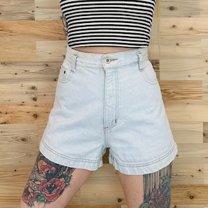 Puede incluir: Pantalones cortos de mezclilla azul claro de cintura alta y dobladillo con vuelta. Los pantalones cortos tienen cierre de botón y cremallera y cinco bolsillos.