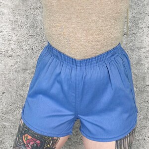 May include: Light blue shorts with an elastic waistband. The shorts are made of a soft fabric and have a relaxed fit. The shorts are a solid color and appear to be vintage.