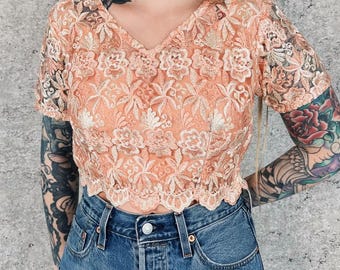 Blusa corta transparente con encaje floral bordado y borde festoneado de malla.