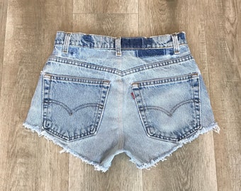 Puede incluir: Pantalones cortos de mezclilla azul claro con bordes deshilachados y bolsillos traseros. Los pantalones cortos tienen cintura alta y un ajuste holgado.