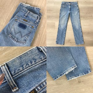 Puede incluir: Vaqueros Wrangler de mezclilla azul claro. Los vaqueros tienen un dise&ntilde;o cl&aacute;sico de cinco bolsillos, una pernera recta y un parche Wrangler en el bolsillo trasero. Los vaqueros est&aacute;n doblados y colocados sobre una superficie de madera clara.