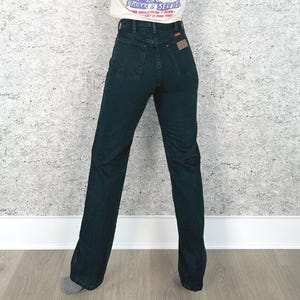 Op de afbeelding: Donkerblauwe denim jeans met een hoge taille en een rechte pijp. De jeans hebben een klassiek ontwerp met vijf zakken en een kleine bruine patch op de achterzak. Het model draagt een wit T-shirt.