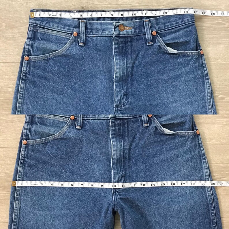 K&ouml;nnte beinhalten: Nahaufnahme von zwei Jeanshosen aus blauem Denim. Die Jeans haben ein klassisches F&uuml;nf-Taschen-Design, Kupfernieten und einen Knopf- und Rei&szlig;verschluss. Ein Ma&szlig;band liegt &uuml;ber dem Bund und zeigt die Bundweite in cm an.
