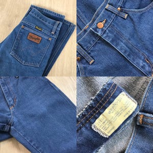 May include: Blue denim Wrangler jeans with a classic five-pocket design. Features a brown leather patch with the Wrangler logo on the back pocket. The jeans have a button and zipper closure and are size 29x32.