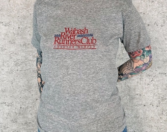 Könnte beinhalten: Ein graues, meliertes Kurzarm-T-Shirt mit dem gestickten roten und blauen Schriftzug Wabash River Runners Club Charter Member auf der Brust. Das Shirt hat einen Rundhalsausschnitt und eine Standardpassform aus weichem, strukturiertem Stoff.