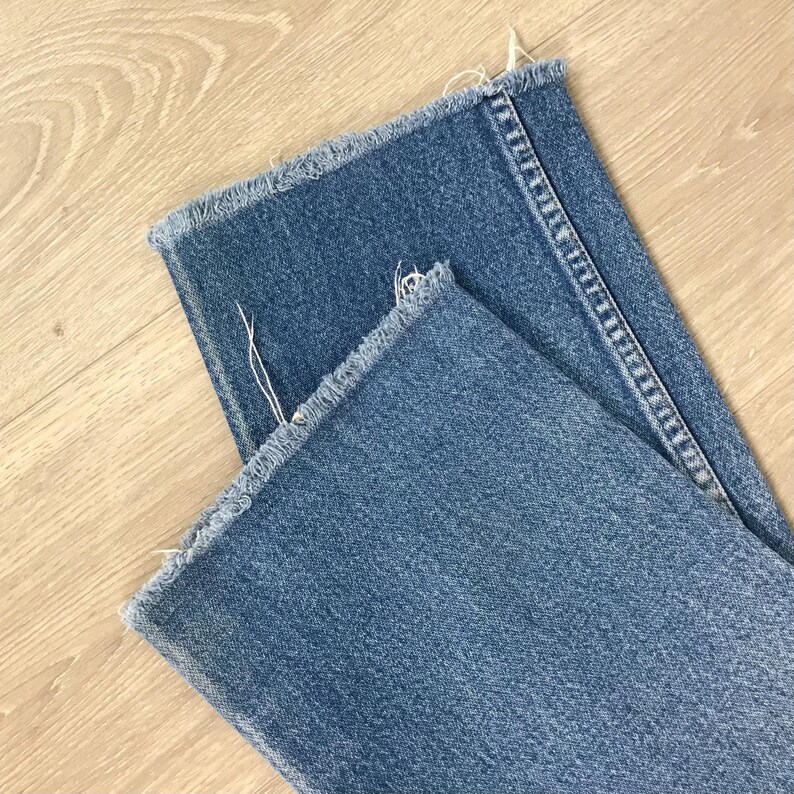 May include: Close-up of blue denim jeans with frayed edges. The jeans are folded, showing the texture and colour of the denim fabric. The frayed edges give the garment a casual, worn appearance.