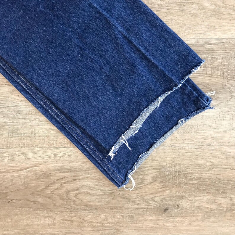 May include: Close-up of the frayed edge of a pair of blue denim jeans.