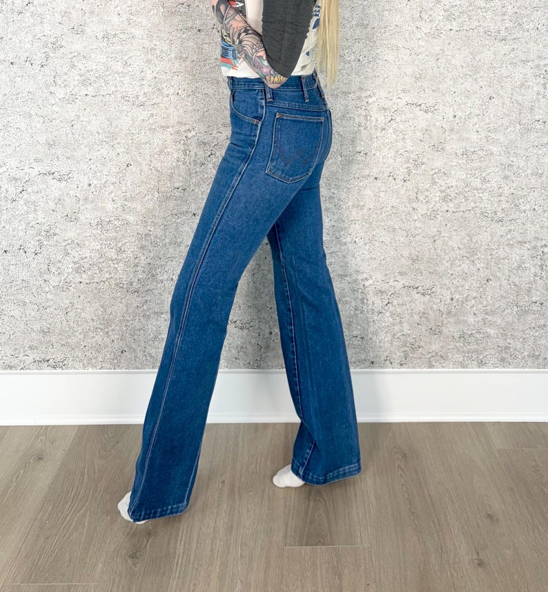 May include: Dark blue denim flared jeans. The jeans have a high waist and a classic five-pocket design. The legs flare out from the knee down, creating a retro silhouette. The jeans are made of a sturdy denim fabric.