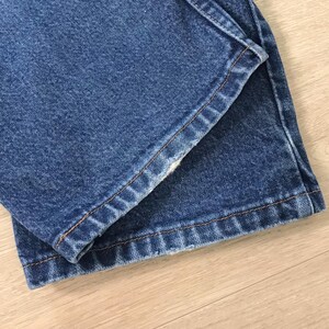 K&ouml;nnte beinhalten: Nahaufnahme einer blauen Jeans aus Denim. Die Jeans ist gefaltet und zeigt den Saum und die Nahtdetails. Der Denim hat ein klassisches, leicht verwaschenes Aussehen. Die N&auml;hte sind in einer kontrastierenden beigen Farbe.