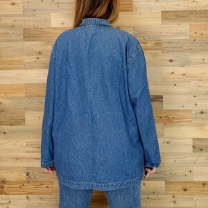 May include: A medium-wash denim jacket and matching jeans. The jacket has long sleeves and a collared neckline with a blue and white plaid pattern. The outfit is displayed against a light brown wood background.