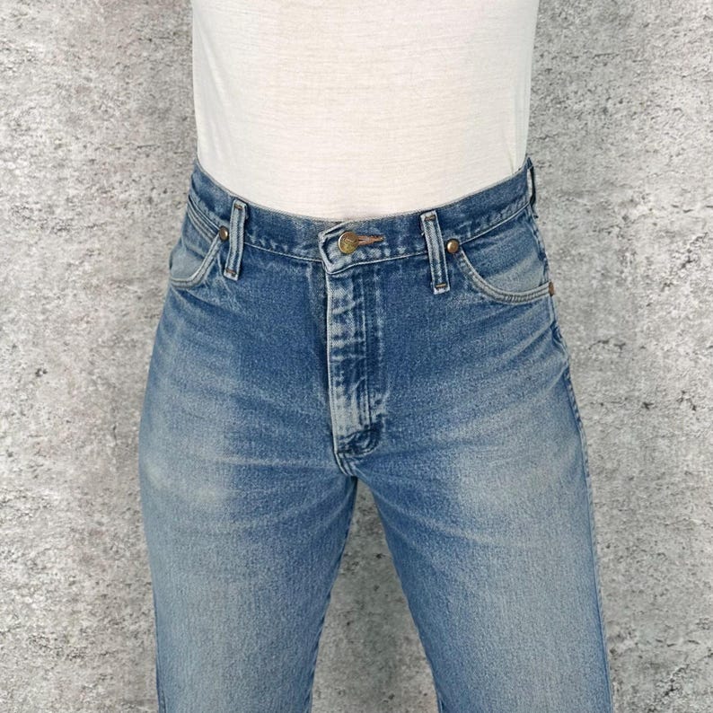 May include: Light blue denim jeans with a button and zip fastening. The jeans feature a classic five-pocket design and a faded wash. The jeans are worn with a white top.