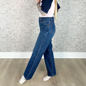 May include: Dark wash denim jeans with a classic straight leg fit. The jeans have a high waist and feature traditional five-pocket styling. The denim is a deep blue color, and the jeans appear to be new or in excellent condition. A timeless wardrobe staple.