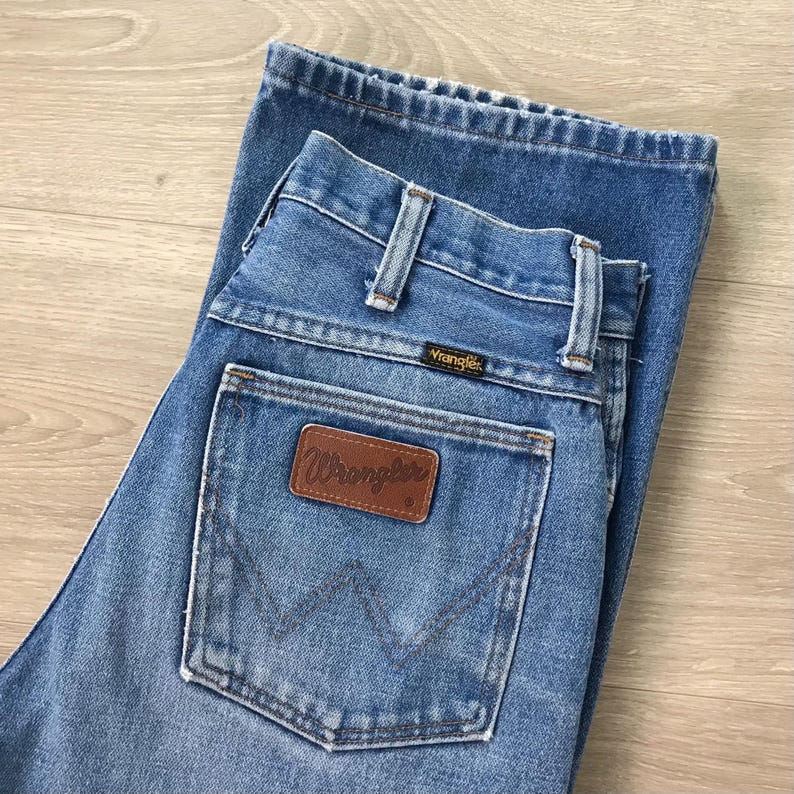 Op de afbeelding: Lichtblauwe spijkerbroek met het Wrangler-logo op de achterzak. De jeans heeft een klassiek ontwerp met vijf zakken, riemlussen en een knoop- en ritssluiting. De jeans is opgevouwen en lijkt in goede staat te verkeren.