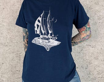 Puede incluir: Camiseta azul marino con un dibujo blanco de un velero. El diseño muestra un velero con velas y dos pájaros. La camiseta está hecha de un material suave y es adecuada para uso casual.