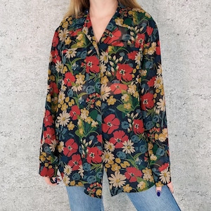 Può includere: Una camicia floreale a maniche lunghe con sfondo blu navy scuro. La camicia presenta un motivo vibrante di papaveri rossi, margherite gialle e altri fiori colorati. La camicia ha un colletto e un'abbottonatura frontale.