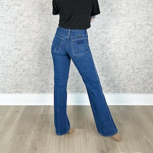 May include: A pair of blue denim flared jeans with a high waist and a small brown leather patch on the back.