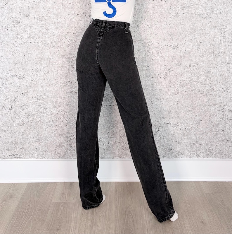 Pu&ograve; includere: Jeans neri a vita alta con gamba dritta. I jeans hanno un classico design a cinque tasche e un lavaggio scuro. La modella indossa una maglietta bianca. I jeans sono realizzati in resistente denim.