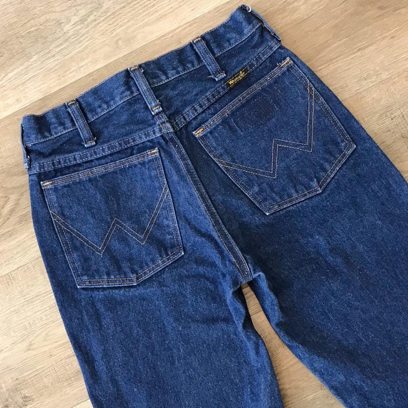 May include: A pair of blue denim jeans with a back pocket featuring a stitched 'W' logo. The jeans have a classic straight leg style.
