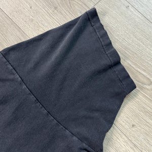 Peut inclure: Gros plan sur une manche de t-shirt gris fonc&eacute;. Le tissu semble l&eacute;g&egrave;rement us&eacute;, avec des coutures visibles et un bord pli&eacute;. La manche est inclin&eacute;e, montrant la texture du mat&eacute;riau.