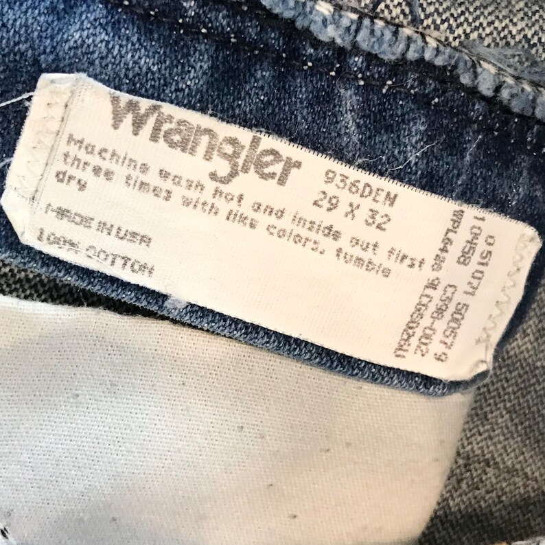 K&ouml;nnte beinhalten: Ein wei&szlig;es Wrangler-Jeans-Pflegeetikett mit dem Text "Machine wash hot and inside out first three times with like colors, tumble dry" und "936DEN 29 x 32" darauf gedruckt. Das Etikett tr&auml;gt au&szlig;erdem die Aufschrift "Made in USA 100% Cotton".