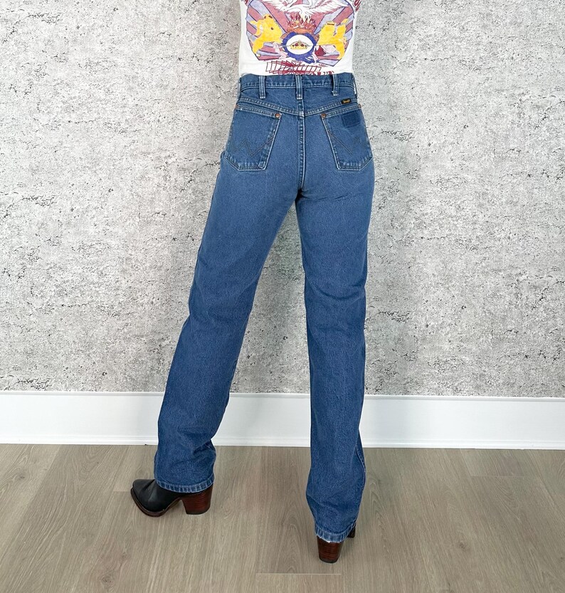 K&ouml;nnte beinhalten: Blaue Jeans aus Denim mit klassischem geradem Bein. Die Jeans hat eine hohe Taille und Taschen vorne und hinten. Das Model tr&auml;gt schwarze Stiefel mit braunem Absatz. Die Jeans hat eine mittlere Waschung.