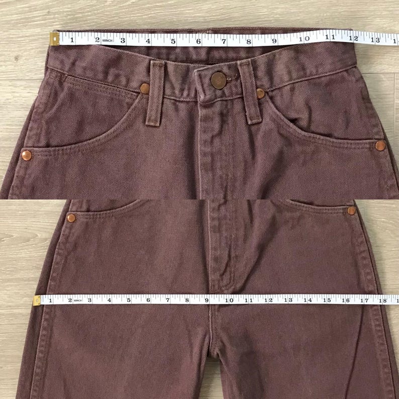 Op de afbeelding: Close-up van een mauvekleurige spijkerbroek. De jeans heeft een knoopsluiting, voor- en achterzakken en koperkleurige klinknagels. De taille meet ongeveer 33 cm breed. De binnenbeenlengte meet ongeveer 46 cm.
