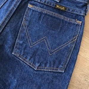 May include: A close-up of a blue denim back pocket with a stitched-in