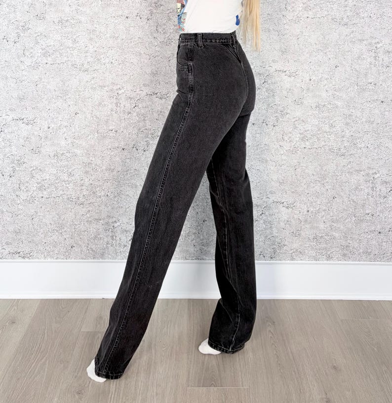 Pu&ograve; includere: Jeans in denim nero con vita alta e gamba larga. I jeans hanno un classico design a cinque tasche e una chiusura con bottone e cerniera. I jeans sono di lavaggio scuro e sembrano essere realizzati in un robusto materiale denim.