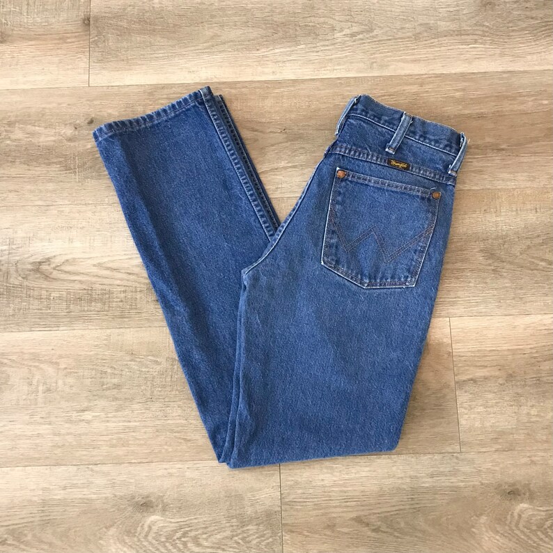 K&ouml;nnte beinhalten: Eine blaue Jeanshose mit einem braunen Leder-Wrangler-Etikett auf der Ges&auml;&szlig;tasche.