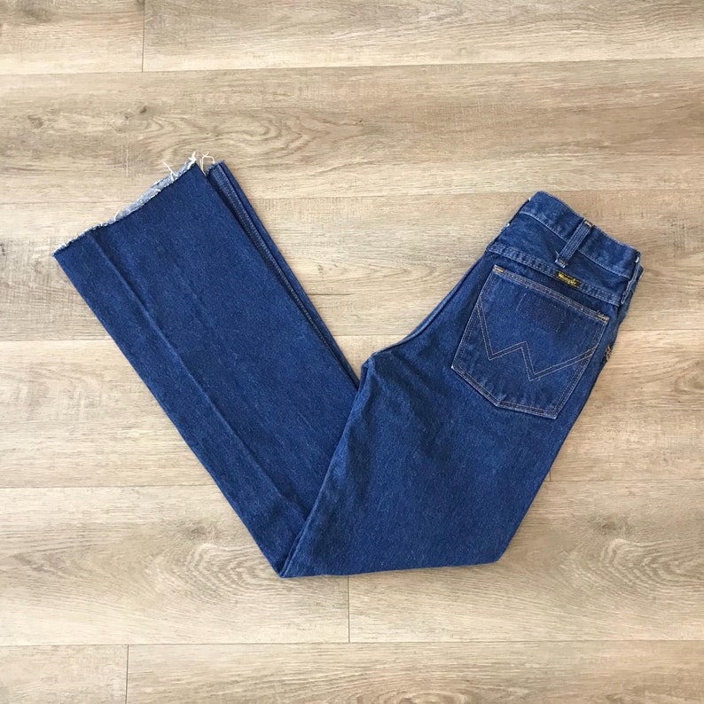May include: A pair of blue denim jeans with a frayed hem and a back pocket with a yellow "Wrangler" logo.