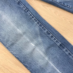 May include: A pair of blue denim jeans featuring a classic five-pocket construction with visible stitching along the seams. The fabric displays a faded wash effect on the thigh area, highlighting the texture of the cotton denim material.