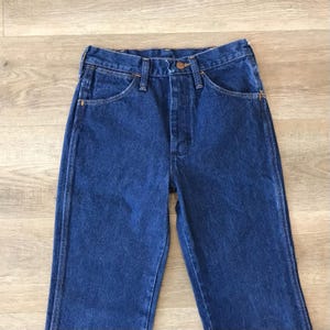 May include: A pair of dark blue denim jeans with a button fly and five pockets.