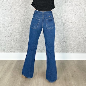 May include: A pair of dark blue denim bell bottom jeans with a high waist. The jeans have a classic five-pocket style and a wide leg opening.