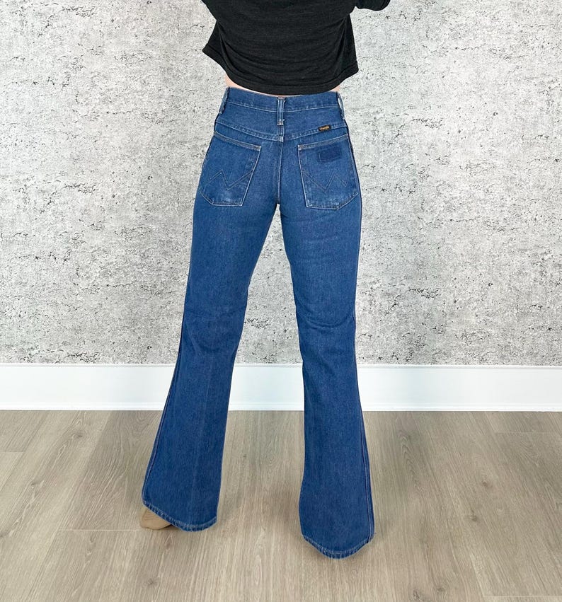 May include: A pair of dark blue denim bell bottom jeans with a high waist. The jeans have a classic five-pocket style and a wide leg opening.