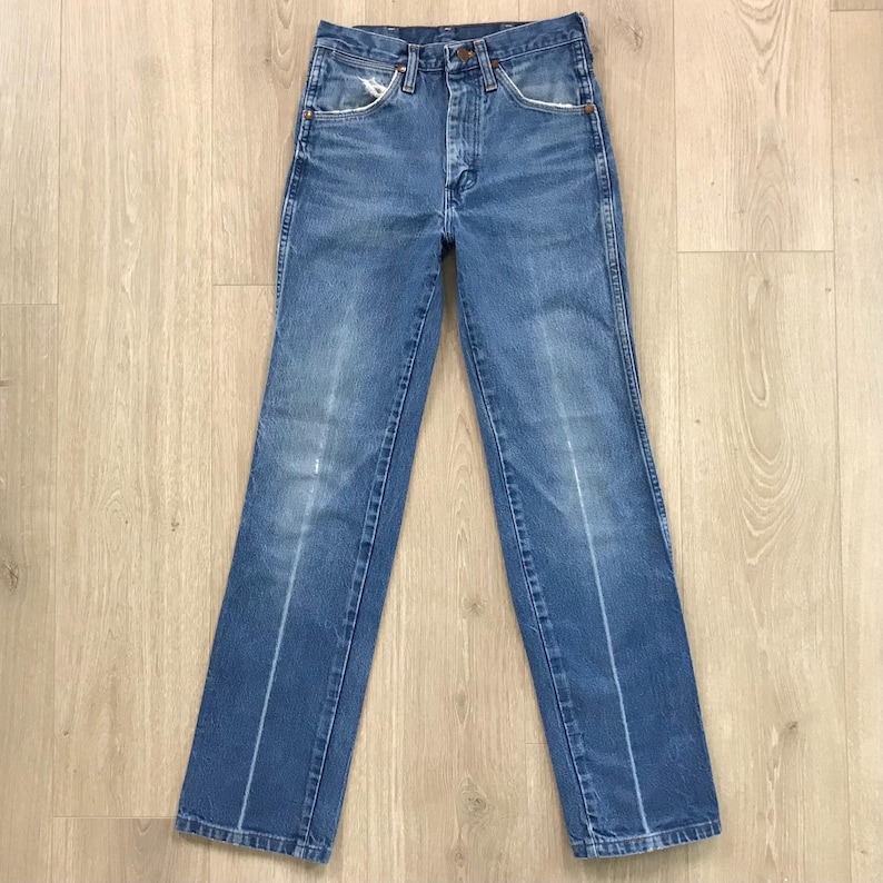 May include: A pair of high-waisted blue denim jeans featuring a classic five-pocket design, a button fly closure, and a straight-leg cut. The fabric displays a faded wash with subtle whiskering details along the thighs and front pockets.