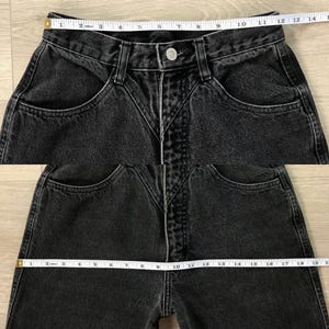 Pu&ograve; includere: Primo piano di jeans neri in denim con vita alta e design unico delle tasche. I jeans hanno una chiusura con bottoni e un classico stile a cinque tasche. Un metro a nastro &egrave; appoggiato sulla vita.
